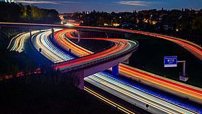 Nighttime photograph of a highway interchange in the Ruhr region; the taillights form red stripes, while the headlights form white stripes.